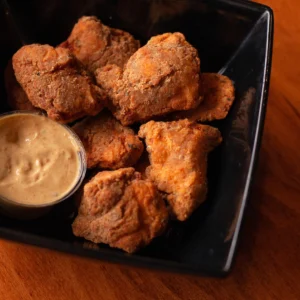 a bowl of fried chicken bites with a cup of dip