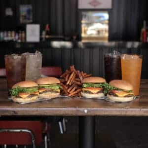 4 cheeseburgers and fries and drinks on a table