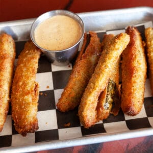 a tray of fried pickles with a cup of dip