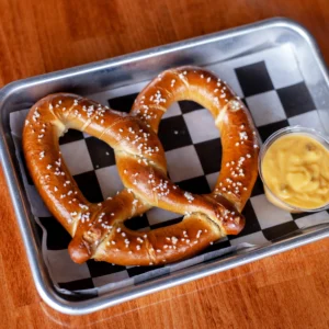 a pretzel on a tray with a cup of beer cheese